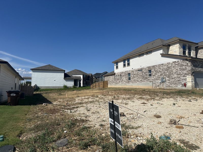 A spacious lot with potential in Royal Crest by Davidson Homes LLC, San Antonio, TX, framed by modern houses under a clear blue sky.