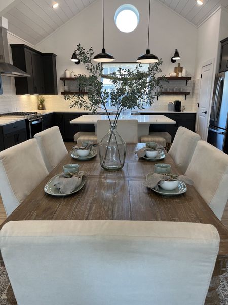A modern dining room with a rustic wooden table, elegant cream chairs, and a stylish kitchen backdrop featuring black cabinetry. A modern dining room with a rustic wooden table, elegant cream chairs, and a stylish kitchen backdrop featuring black cabinetry.