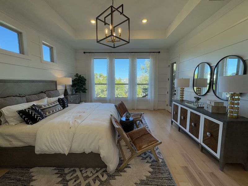 A luxurious bedroom featuring a tray ceiling, large windows, stylish lighting, and elegant decor with a comfy bed and mirrored accents. A luxurious bedroom featuring a tray ceiling, large windows, stylish lighting, and elegant decor with a comfy bed and mirrored accents.