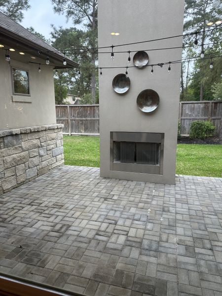A chic outdoor patio featuring string lights, decorative wall art, and a modern fireplace.