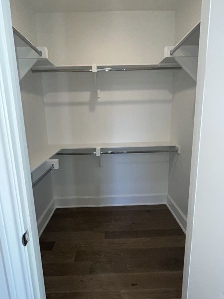 A spacious walk-in closet with sleek shelving and dark wood flooring, offering ample storage space for any wardrobe. A spacious walk-in closet with sleek shelving and dark wood flooring, offering ample storage space for any wardrobe.
