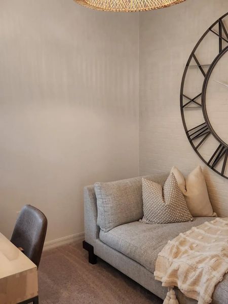 A cozy corner features a gray chaise lounge, oversized clock, and plush throw, creating a serene and stylish retreat.