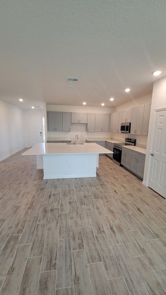 A contemporary kitchen with sleek gray cabinets, a central island, and wood-like tile flooring.