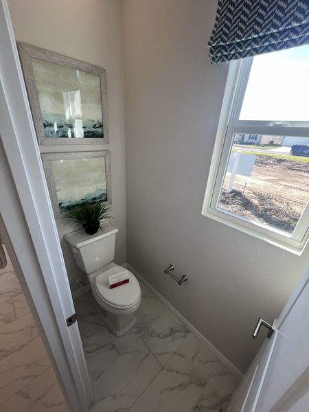 A chic bathroom with marble flooring, wall art, and a window with patterned shades.
