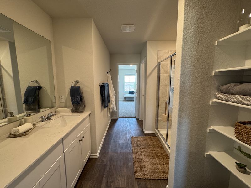 Modern bathroom featuring dual sinks, elegant wood flooring, and cozy shelving with plush towels.
