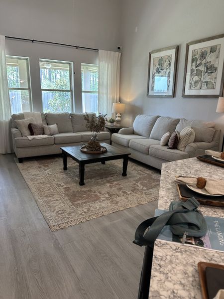 A cozy living room featuring plush sofas, elegant artwork, and a soft rug, with natural light streaming through large windows.
