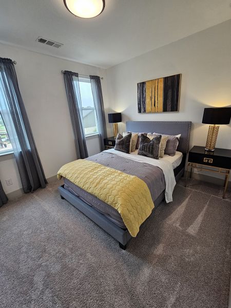 A cozy bedroom with a tufted bed, gold accents, plush carpeting, and natural light from large windows.