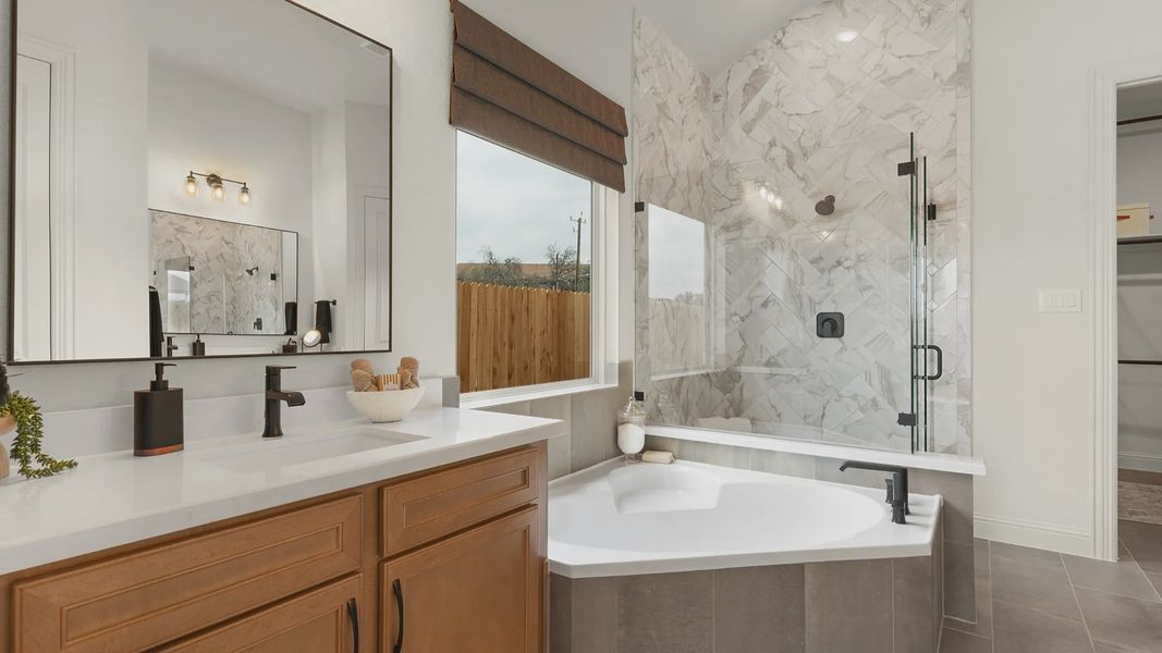 Owner’s bath features a modern design with a separate garden tub, frameless glass shower, and ceramic tile.