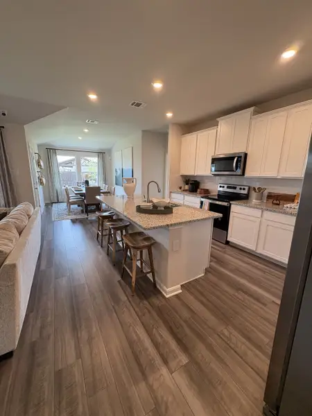 A modern kitchen with sleek white cabinets, granite countertops, and a spacious island, opening to a bright dining area.