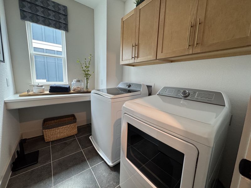 A modern laundry room with sleek appliances, light wood cabinets, and a bright window offering natural light.