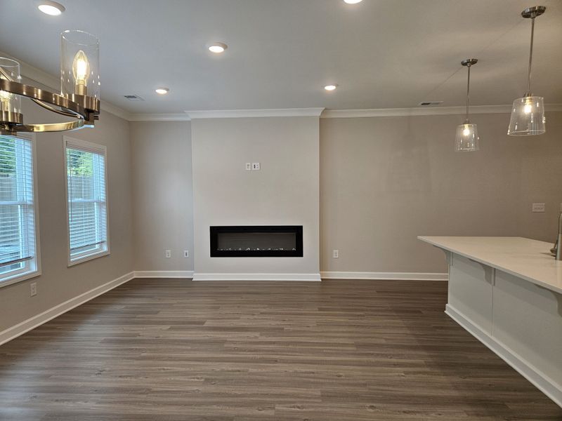 A modern living space featuring wood floors, a sleek electric fireplace, and elegant pendant lighting for a cozy ambiance.