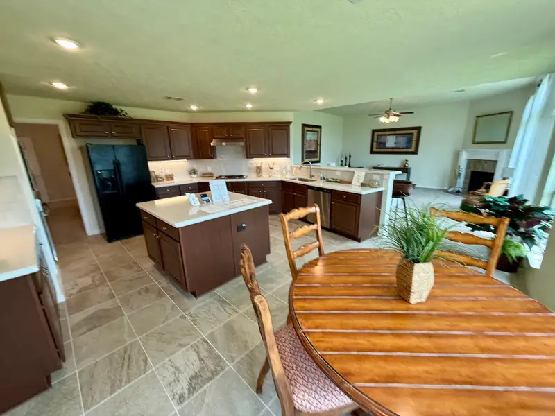 Spacious kitchen with wooden cabinets, a central island, and an open dining area featuring a round wood table with greenery.