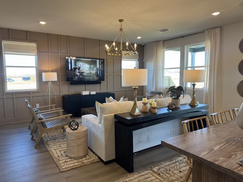 A cozy living room featuring a large wall-mounted TV, elegant chandelier, and comfortable seating with warm, neutral decor.