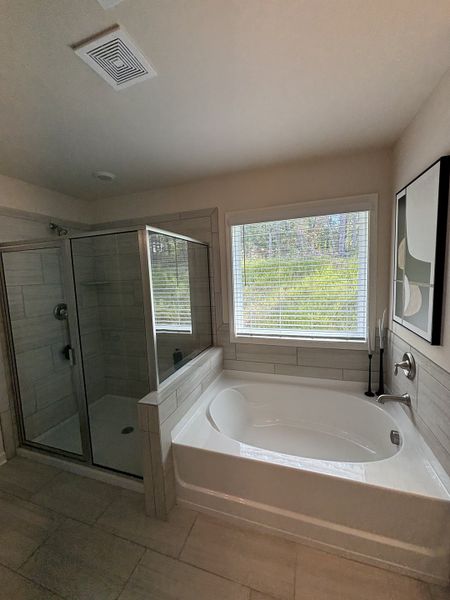 A chic bathroom featuring a glass shower, large bathtub, and modern tile accents with natural light streaming in.