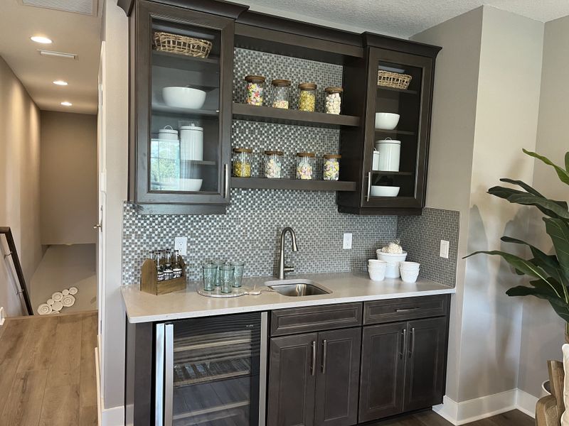 A chic wet bar with dark cabinetry, glass shelving, mosaic backsplash, and a built-in wine fridge for a modern touch.