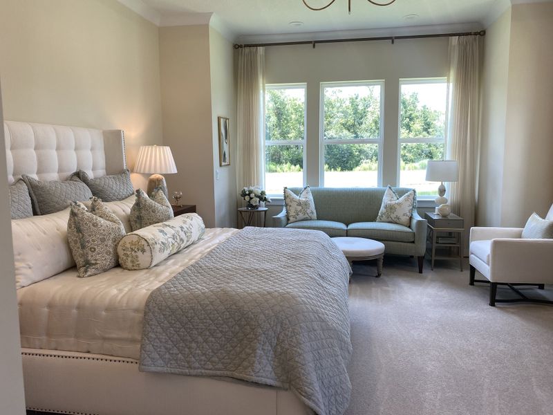 A serene bedroom with an upholstered bed, elegant seating area, and large windows with a nature view.