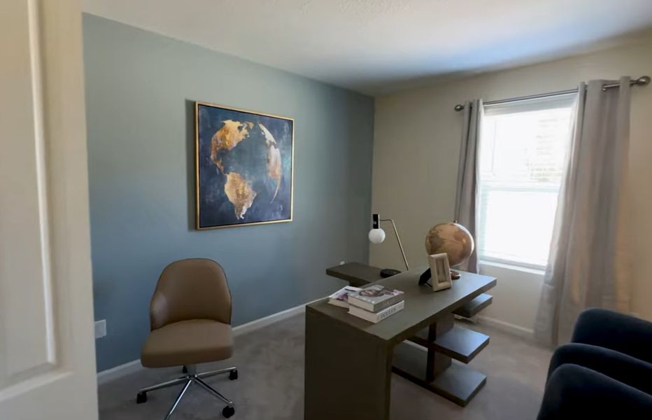 A cozy office space with a sleek desk, globe, and artistic wall art, complemented by natural light from a large window.