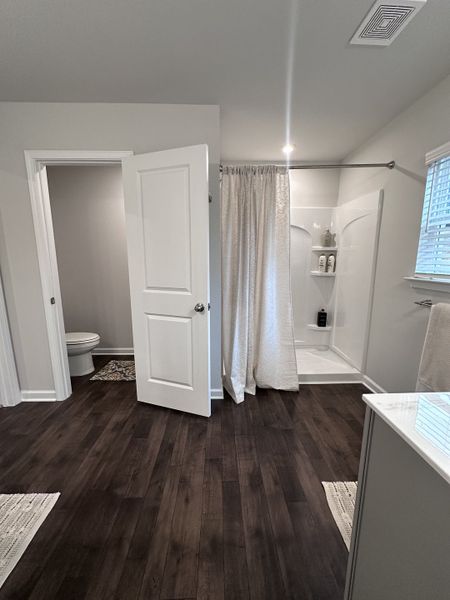 A sleek bathroom with dark wood floors, a shower with a curtain, and a separate toilet area for privacy.