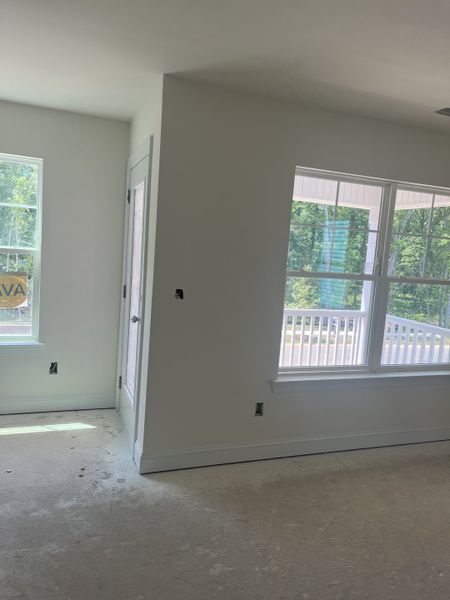 A bright, unfinished room with large windows offering a view of lush greenery and a balcony. A bright, unfinished room with large windows offering a view of lush greenery and a balcony.