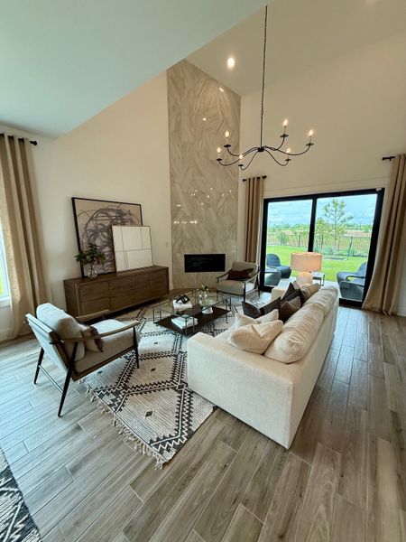 A spacious living room featuring a modern chandelier, stylish furniture, and large windows opening to a lush outdoor view.