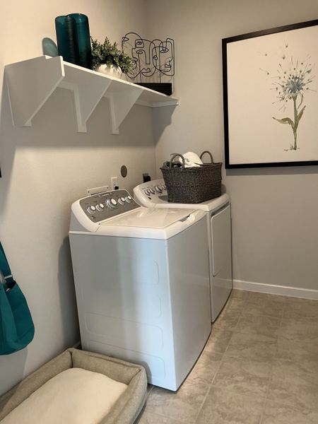 A functional laundry room featuring modern appliances, decorative shelving, and a charming wall art piece.