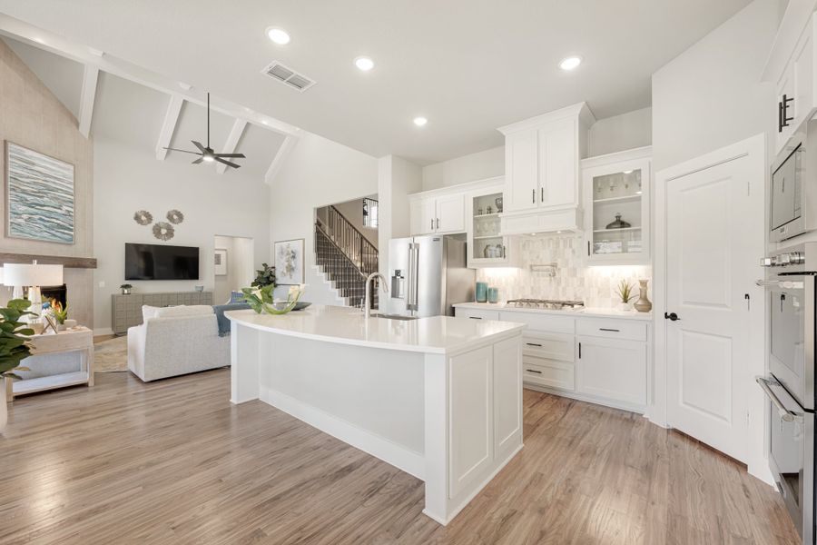 Open-concept kitchen with white cabinets, large island, and hardwood floors, open to living room with fireplace and vaulted ceiling.