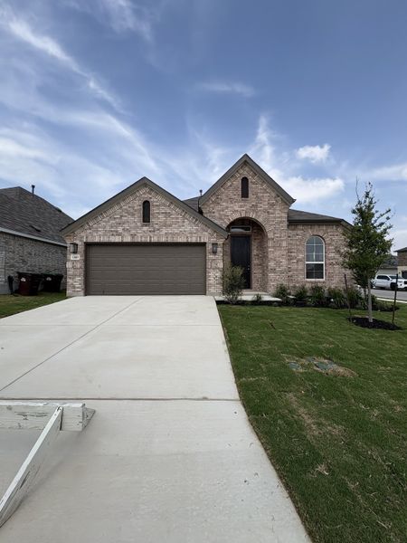 Charming brick home with a spacious driveway and lush lawn in Veranda by Brightland Homes (San Antonio, TX).