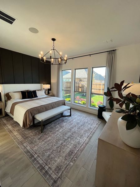 A cozy bedroom with a stylish chandelier, dark feature wall, and large windows overlooking a lush garden.