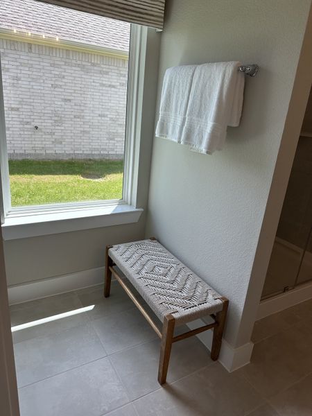 A cozy corner with a woven bench by the window, soft towels, and light tiled flooring. A cozy corner with a woven bench by the window, soft towels, and light tiled flooring.