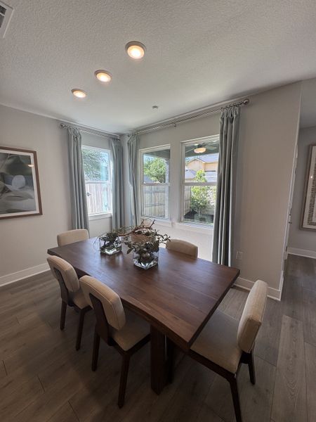 A cozy dining room with a wooden table, elegant chairs, and large windows framed by soft curtains.