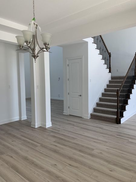A modern entryway with wood flooring, a sleek chandelier, and a carpeted staircase leading upwards.