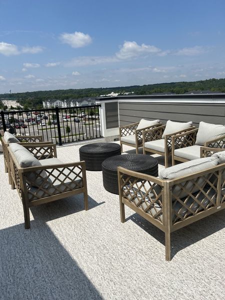 A stylish rooftop patio with wooden lattice furniture and round wicker tables, offering expansive views under a clear sky.