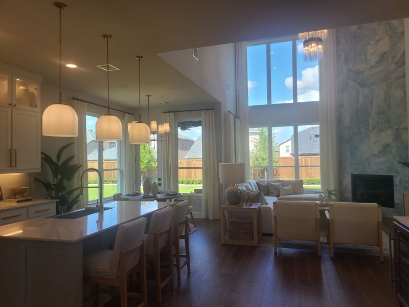 A bright, open-concept living space with high ceilings, modern lighting, and a large window overlooking the backyard.