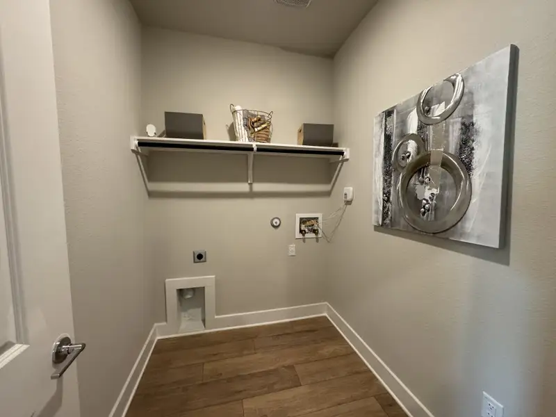 A modern laundry room with wood flooring, wall-mounted shelving, and abstract artwork for an elegant touch.
