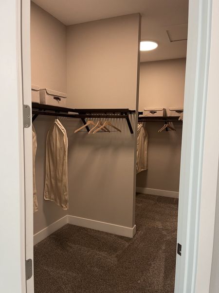 A spacious walk-in closet with beige walls, carpeted flooring, and ample shelving and storage boxes.