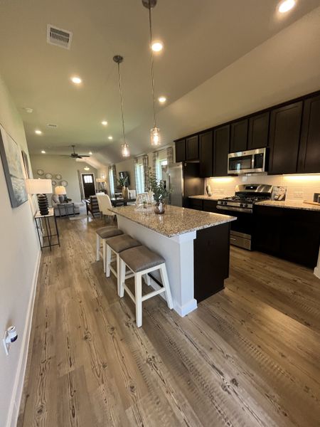 A modern kitchen with dark cabinetry, granite island, pendant lighting, and open layout featuring wood flooring.