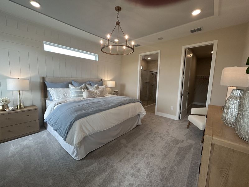 A serene bedroom with cozy bedding, soft lighting, plush carpet, and an elegant chandelier, leading to a walk-in shower.