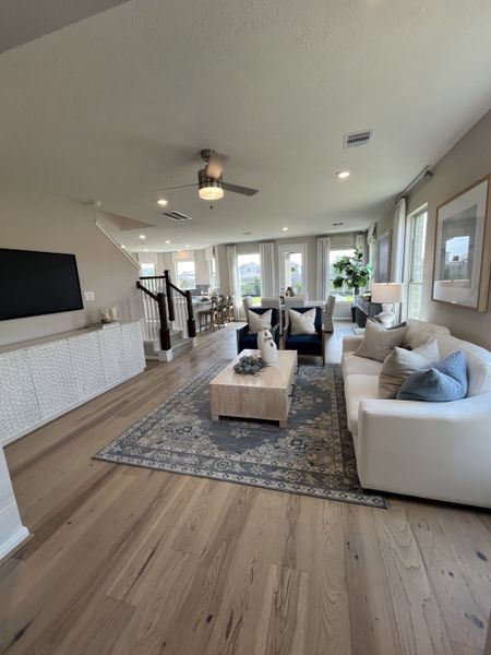 Modern living room with light wood floors, plush seating, elegant decor, and abundant natural light, creating a cozy ambiance.