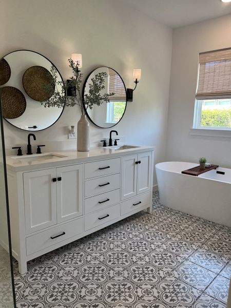 A stylish bathroom with patterned tile flooring, dual round mirrors, and a sleek white vanity. A stylish bathroom with patterned tile flooring, dual round mirrors, and a sleek white vanity.