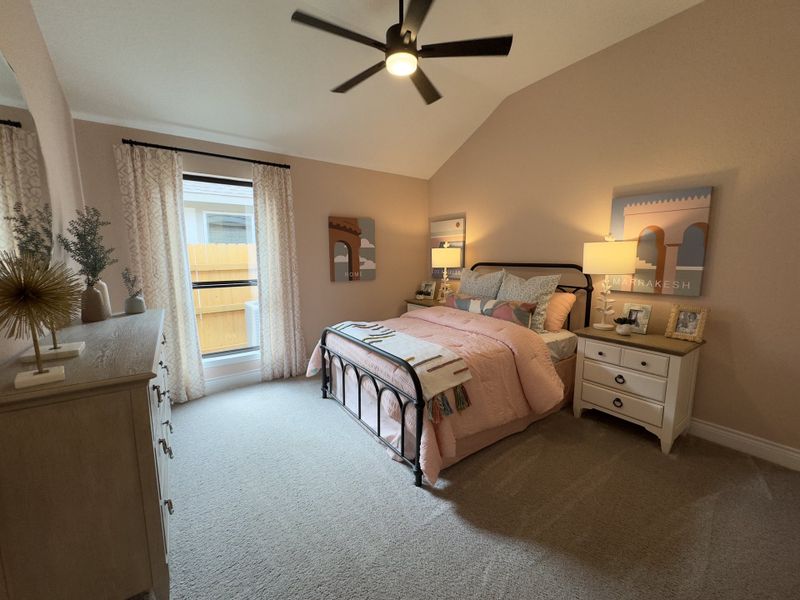 A cozy bedroom with soft pink accents, a wrought iron bed, and elegant decor, complemented by a ceiling fan and natural light.