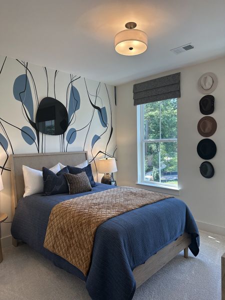 A cozy bedroom with abstract wall art, blue bedding, and stylish decor featuring a collection of hats and modern lighting.