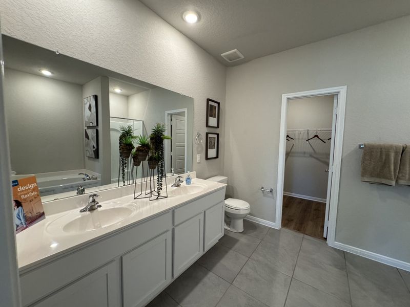 A sleek bathroom featuring a double vanity, large mirror, and a walk-in closet with modern decor.