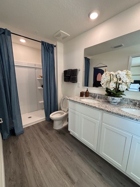 A stylish bathroom with a granite vanity, white cabinetry, and a spacious walk-in shower in Avian Pointe Townhomes by D.R. Horton (Apopka, FL).