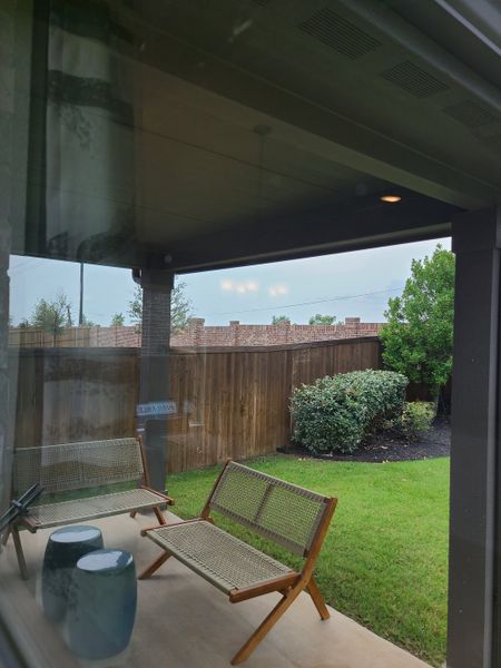 A cozy patio with woven chairs and side tables overlooking a green yard and wooden fence. A cozy patio with woven chairs and side tables overlooking a green yard and wooden fence.