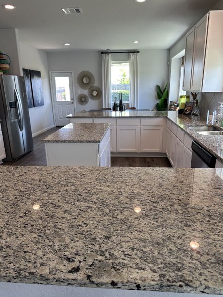 A modern kitchen featuring granite countertops, white cabinetry, and stainless steel appliances.