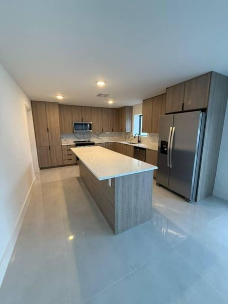 A modern kitchen featuring sleek wooden cabinetry, a large island with white countertops, and stainless steel appliances.