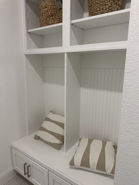 A cozy mudroom nook with striped cushions, wicker baskets, and sleek white cabinetry. A cozy mudroom nook with striped cushions, wicker baskets, and sleek white cabinetry.