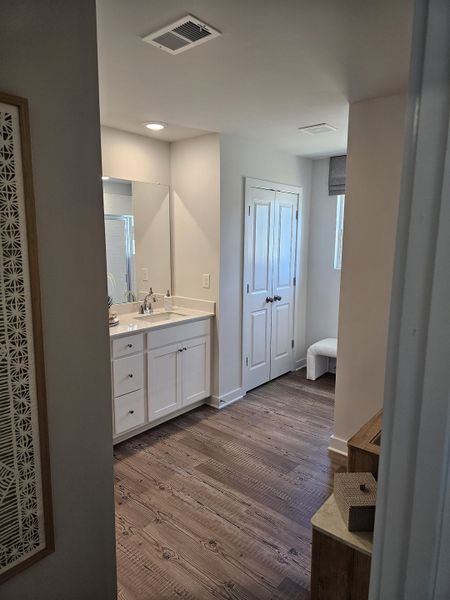 A bright bathroom with white cabinetry and wood flooring, featuring elegant fixtures and a cozy seating nook. A bright bathroom with white cabinetry and wood flooring, featuring elegant fixtures and a cozy seating nook.