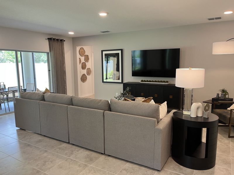 A modern living room featuring a cozy gray sectional, wall-mounted TV, and sleek decor with natural light flowing in.