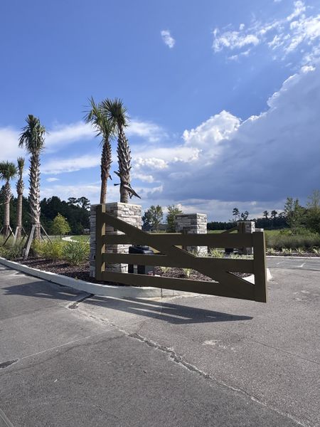 A gated entrance with palm trees and modern stone pillars in Jennings Farm by Dream Finders Homes (Middleburg, FL).